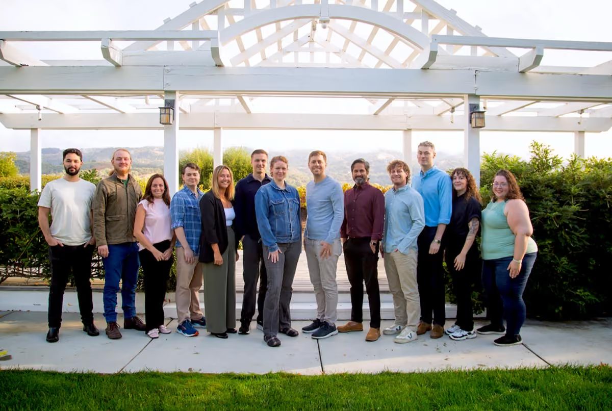 Twelve First Bite teammates standing in a row outdoors in front of a white pergola, with green hills behind them
