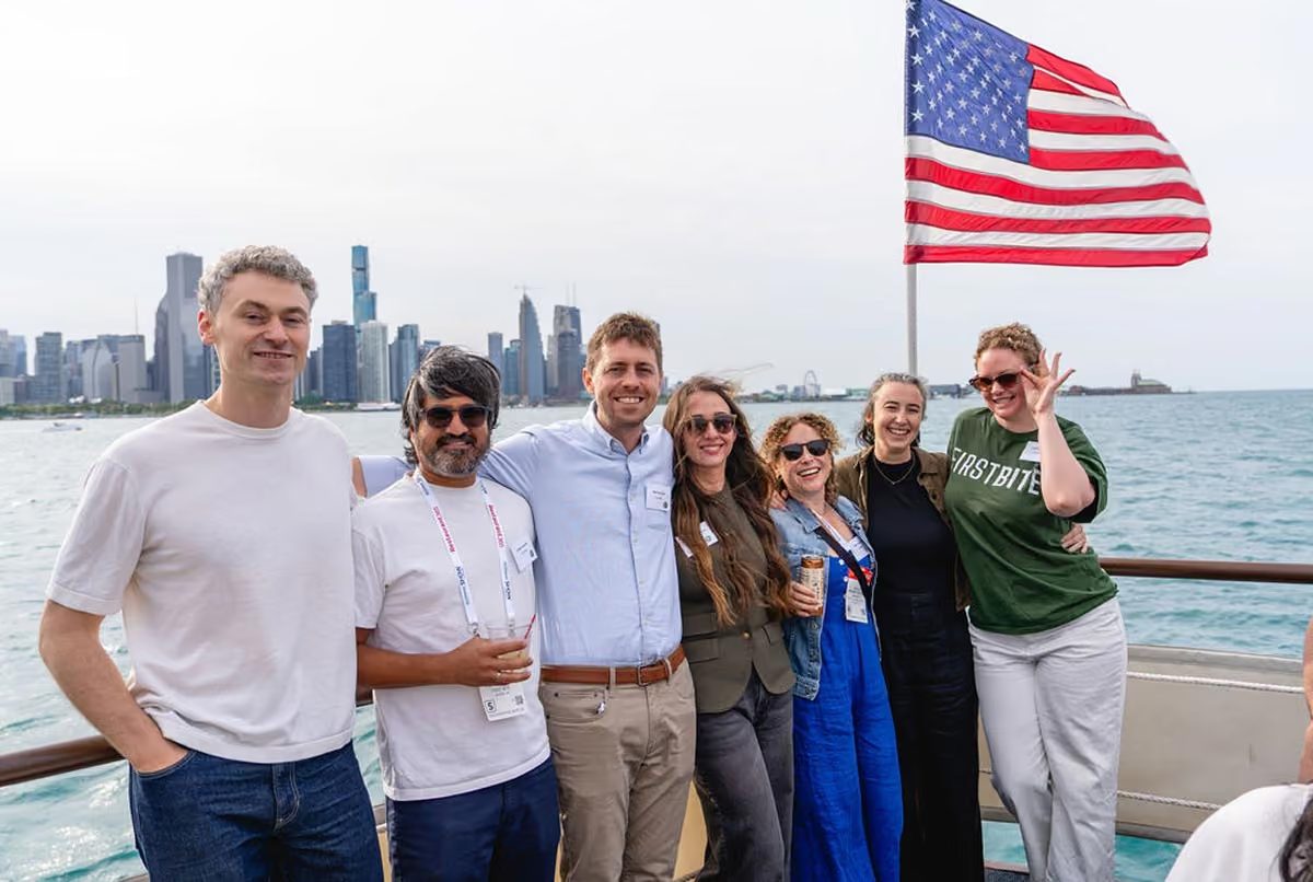 Seven teammates posing together on a boat deck, with the Chicago skyline and an American flag behind them